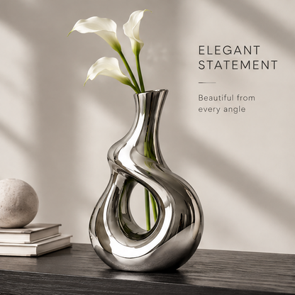 Elegant statement mirror silver vase with white calla lilies displayed on a dark wooden console beside stacked books and a stone sphere